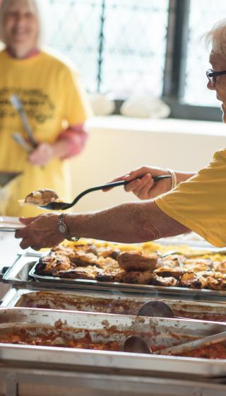 Older volunteer serving food to a young person