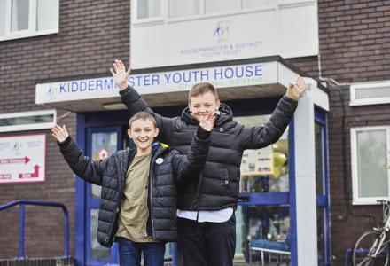Two smiling boys holding their hands in the air in front of their youth club