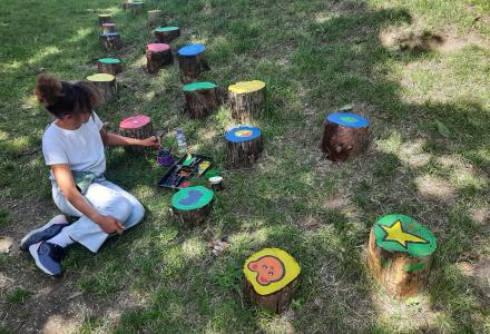 Girl outdoors painting tree stumps