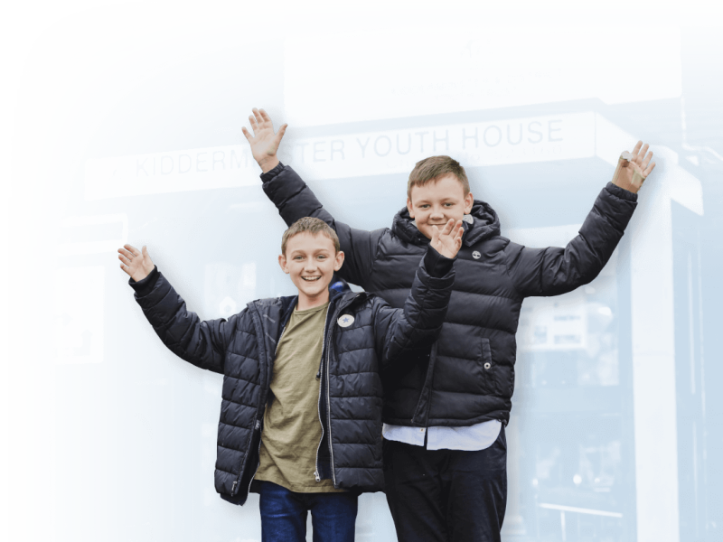 Two smiling boys holding their hands in the air in front of their youth club