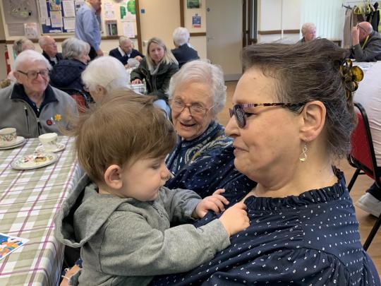 Elderly woman sitting a tea party, holding a toddler in her arms