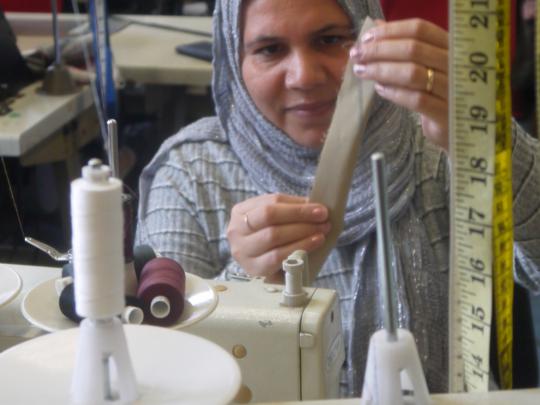 Woman sitting at a sewing machine, folding a strip of fabric